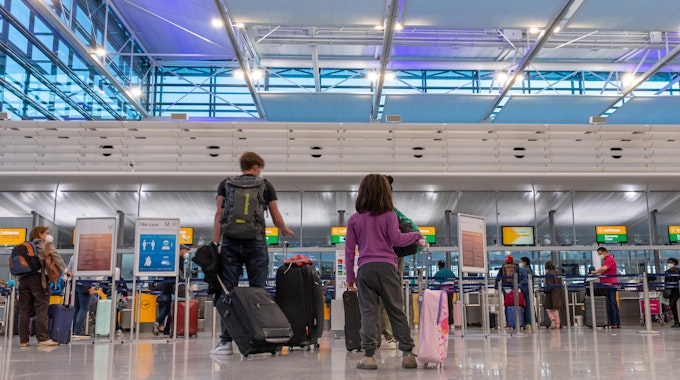 Passagiere stehen am Flughafen München an einem Check-In-Schalter.