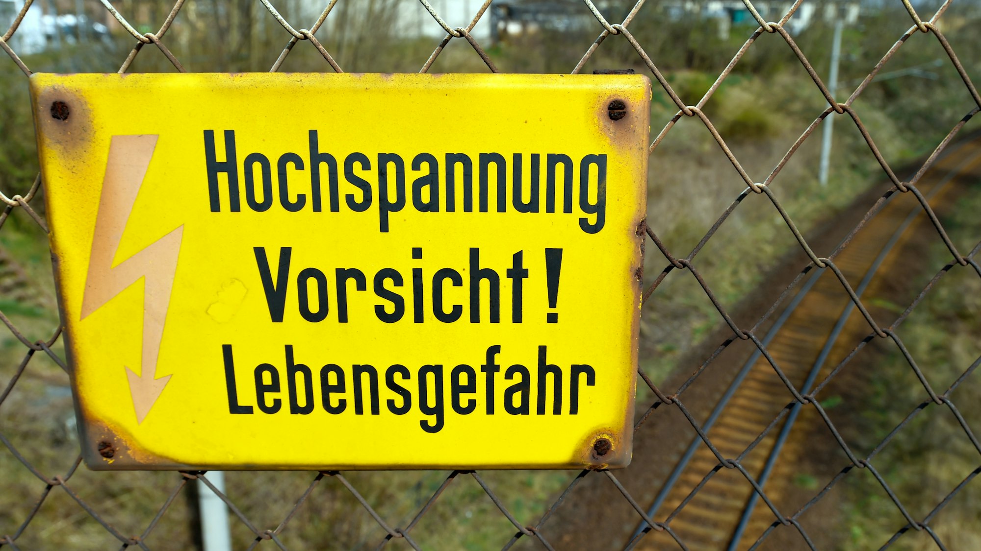 Das Symbolfoto zeigt ein deutsches Hinweisschild, das an einem Zaun hängt. Auf dem steht mit schwarz auf gelbem Untergrund „Hochspannung Vorsicht! Lebensgefahr”.