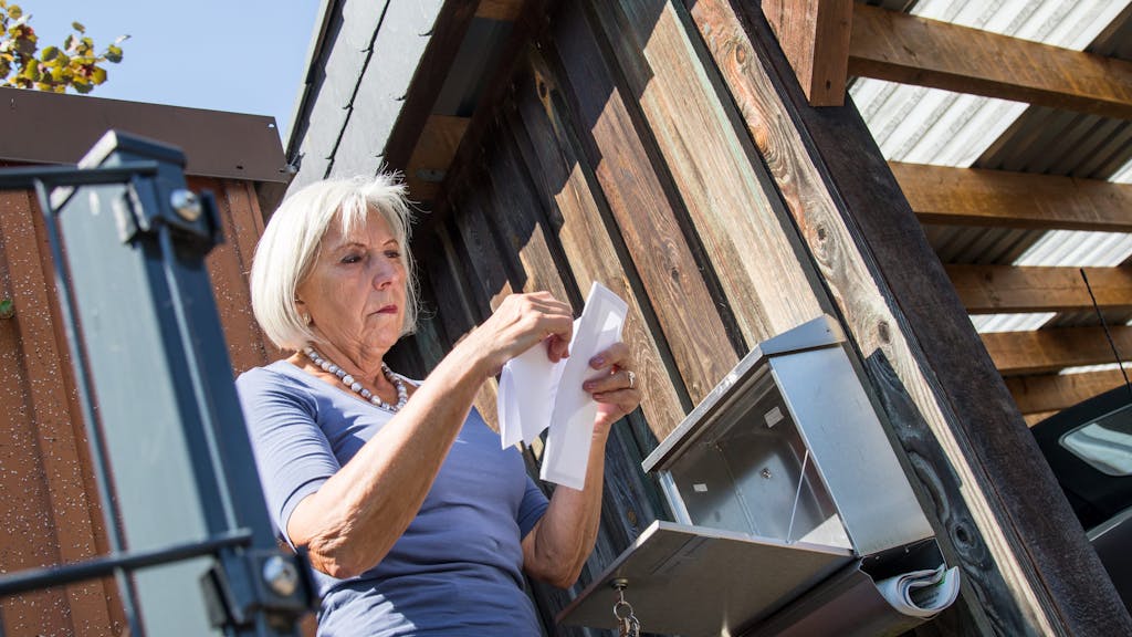 Eine ältere Dame steht am Briefkasten und sieht ihre Post durch. (Symbolfoto).