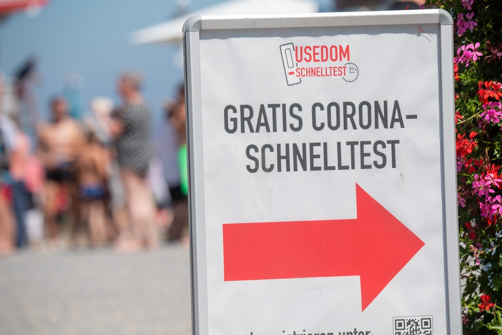 Passanten gehen am 13.07.2021 an einem Hinweisschild mit dem Schriftzug „Gratis Corona Schnelltest“ in Zinnowitz vorbei.