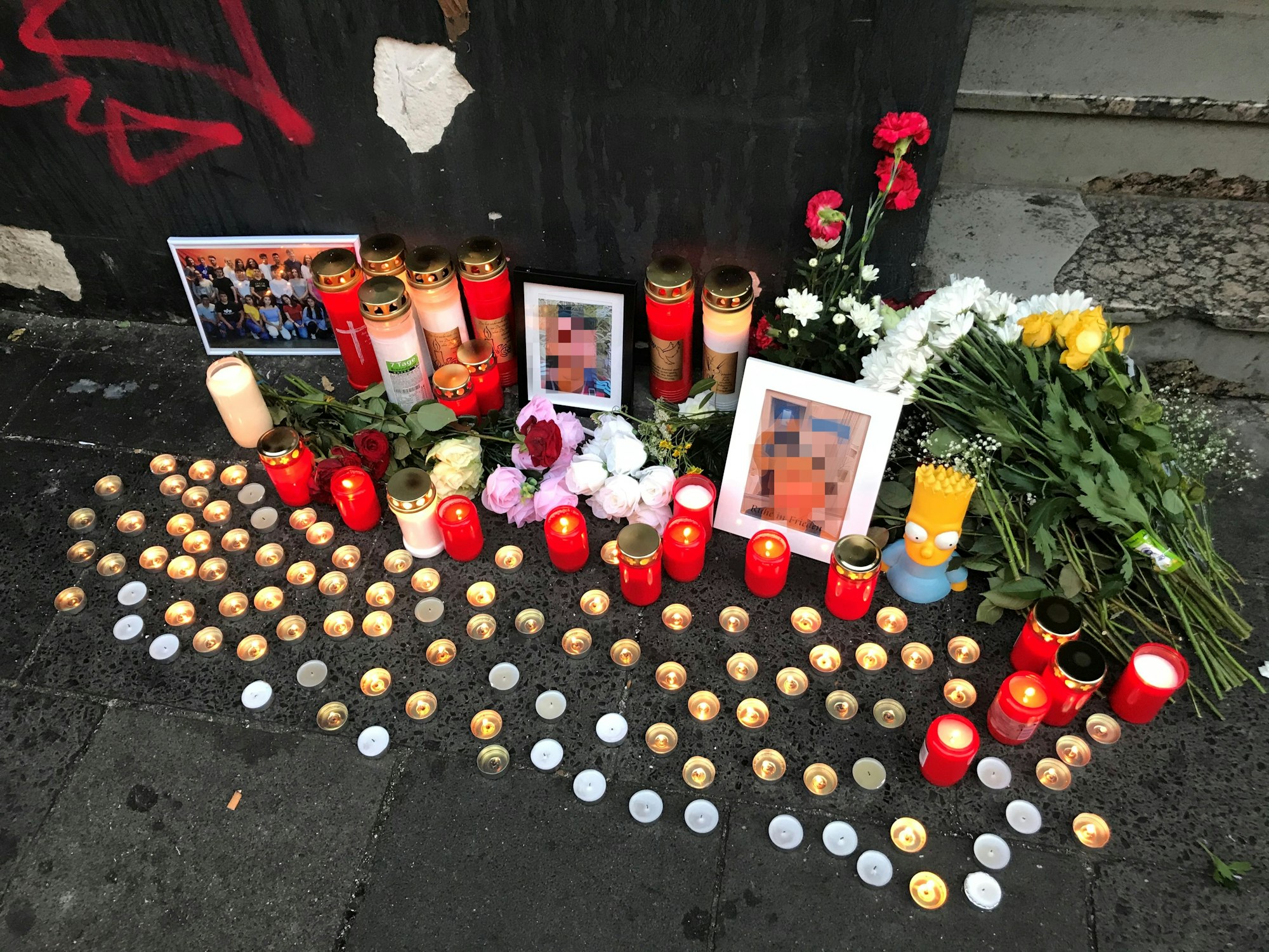Auf dem Asphalt sind Kerzen und Blumen niedergelegt, auch Fotos des Opfers sind zu sehen.