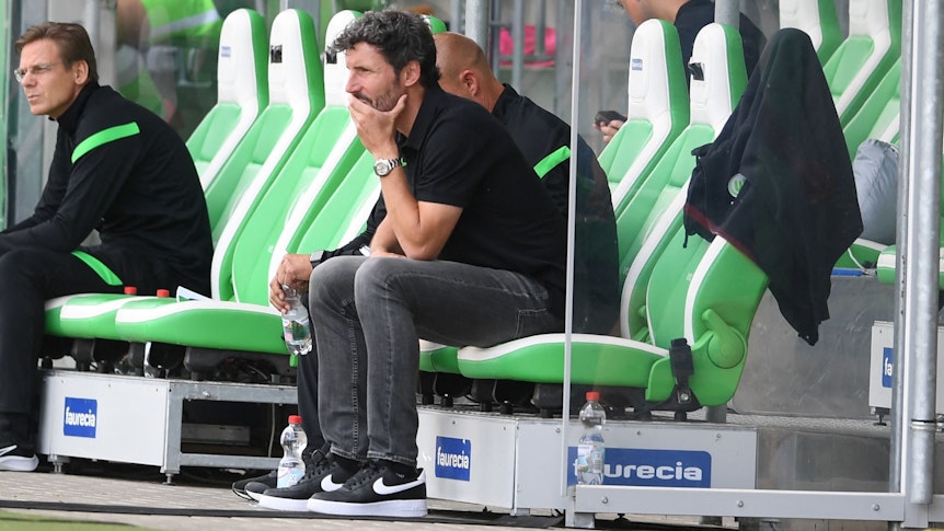 Mark van Bommel sitzt genervt auf der Trainerbank des VfL Wolfsburg.