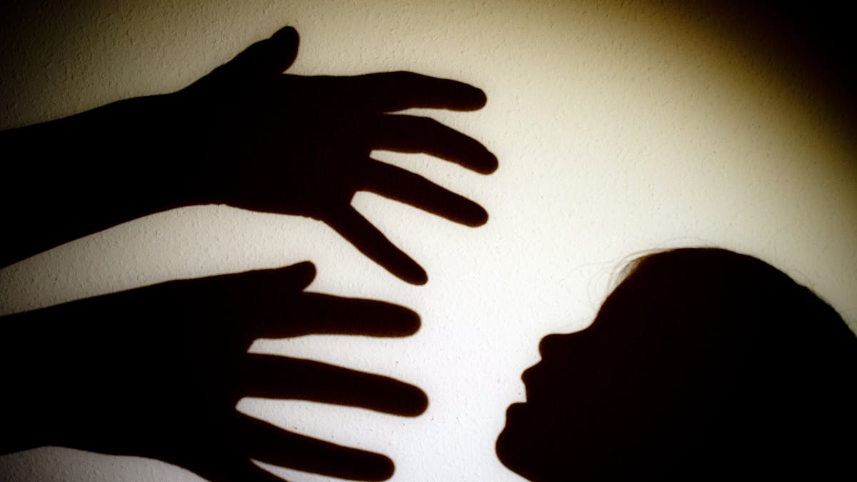 Schatten von Händen einer erwachsenen Person und dem Kopf eines Kindes an einer Wand eines Zimmers.