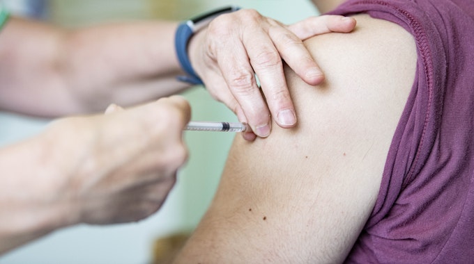 Ein Arzt impft ein Kind mit einer Nadel in den Oberarm.