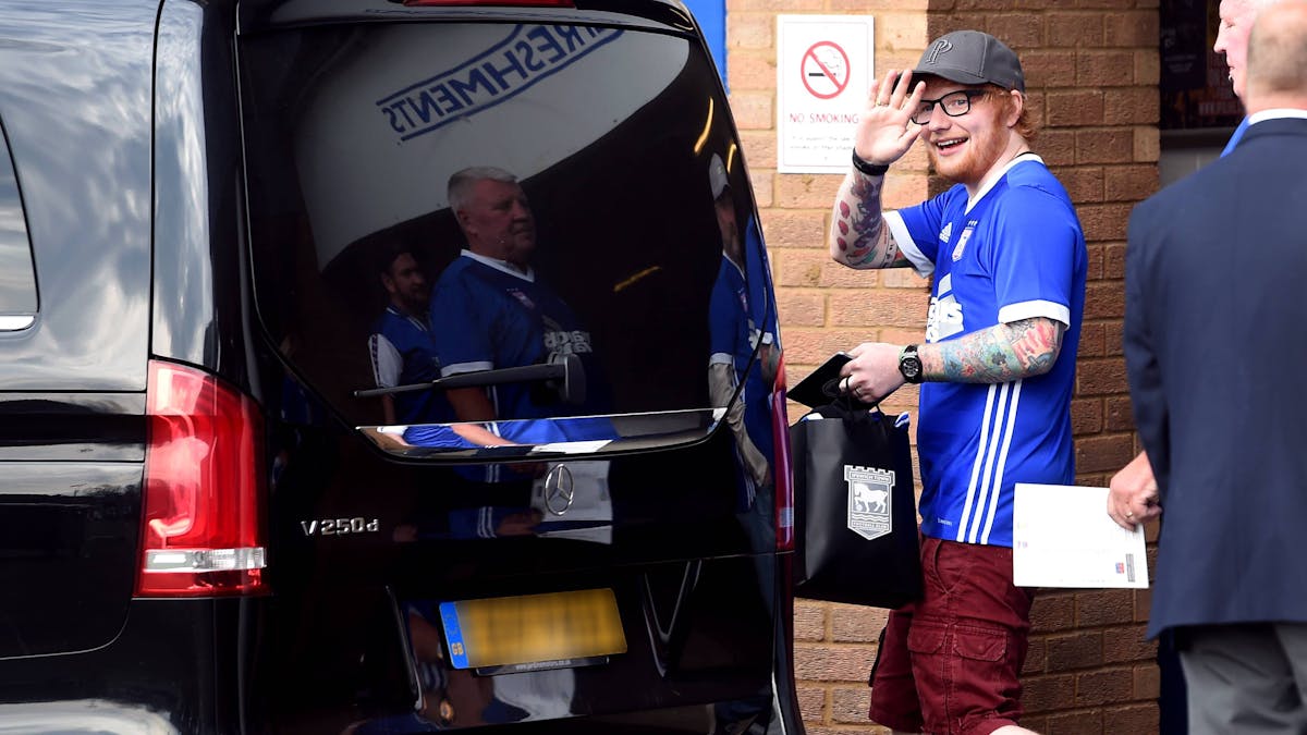 Ed Sheeran winkt mit einem Trikot des englischen Drittligisten Ipswich Town in die Kamera.