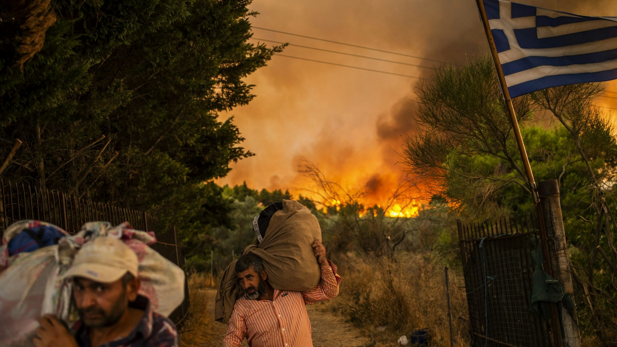 Menschen versuchen Teile ihrer Habe in Sicherheit zu bringen, während ein Waldbrand in einem Waldgebiet nördlich von Athen wütet.