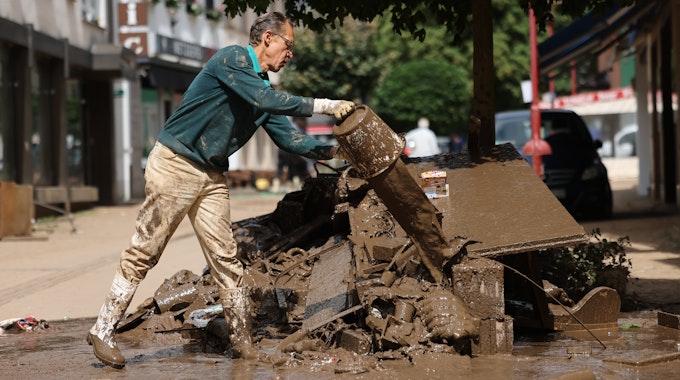 Das Foto zeigt einen Mann, der Schlammreste aus einem Haus auf einem Haufen von Schutt ausgießt.