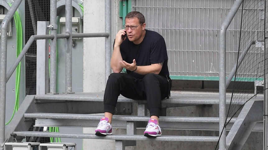 Gladbach-Manager Max Eberl sitzt auf einer Metalltreppe im Borussia-Park, derweil telefoniert er mit seinem Smartphone, mit der linken Hand gestikuliert er.