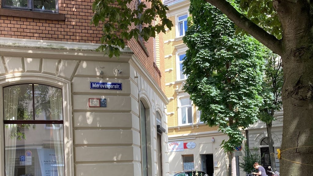 In der Merowingerstraße gibt es ein Schild mit anderer Schreibweise, hier heißt es Merovingerstraße. Bei den blauen Straßennamensschildern handelt es sich um eine historische Beschilderung.