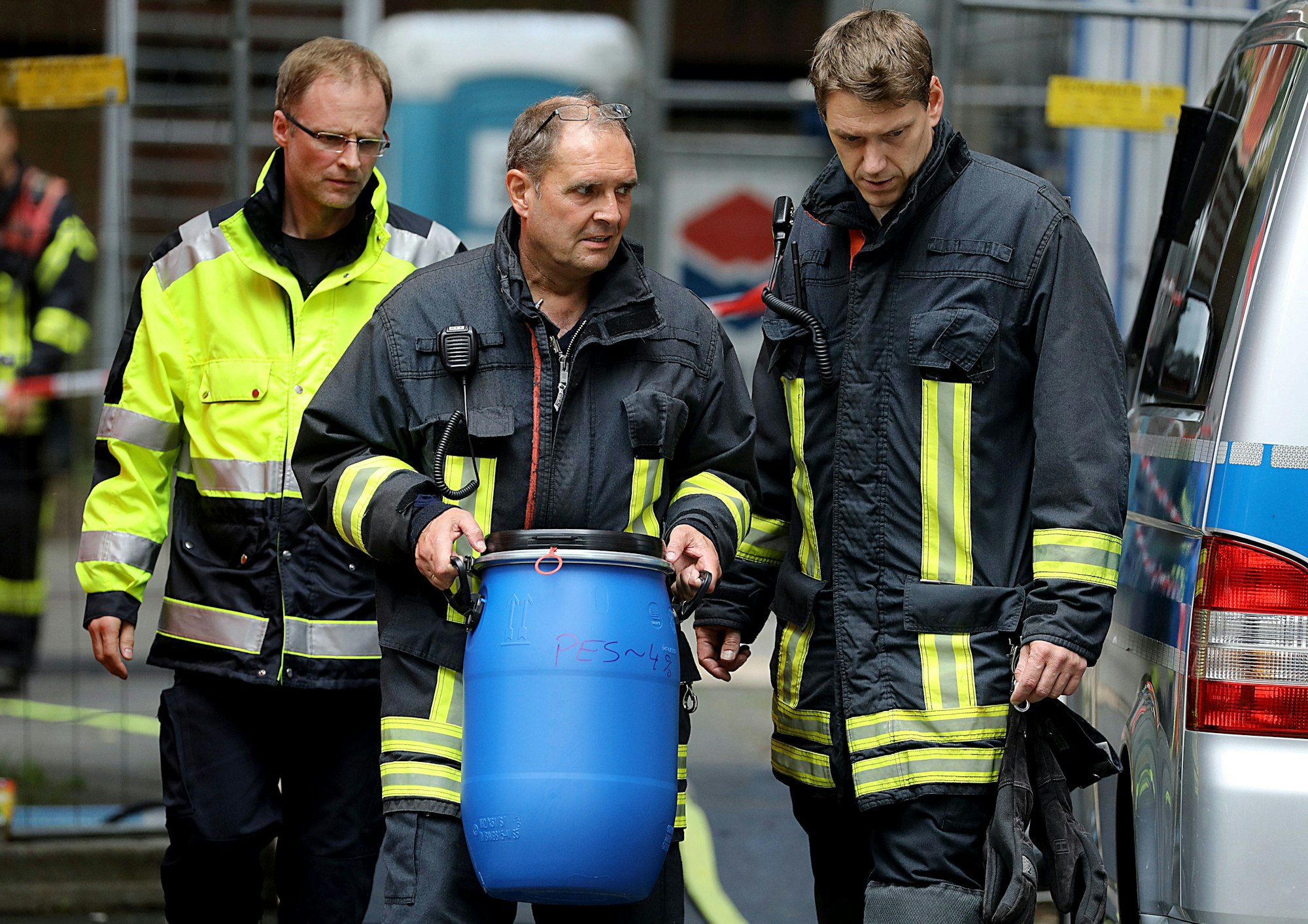 Ein Feuerwehrmann trägt vor dem Wohnkomplex in Köln-Chorweiler eine Tonne heraus.