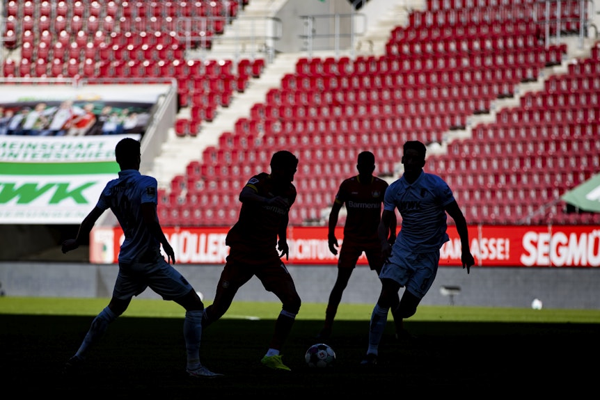 Spieler des FC Augsburg und Bayer 04 Leverkusen sind bei einem Geisterspiel als Silhouette zu sehen.