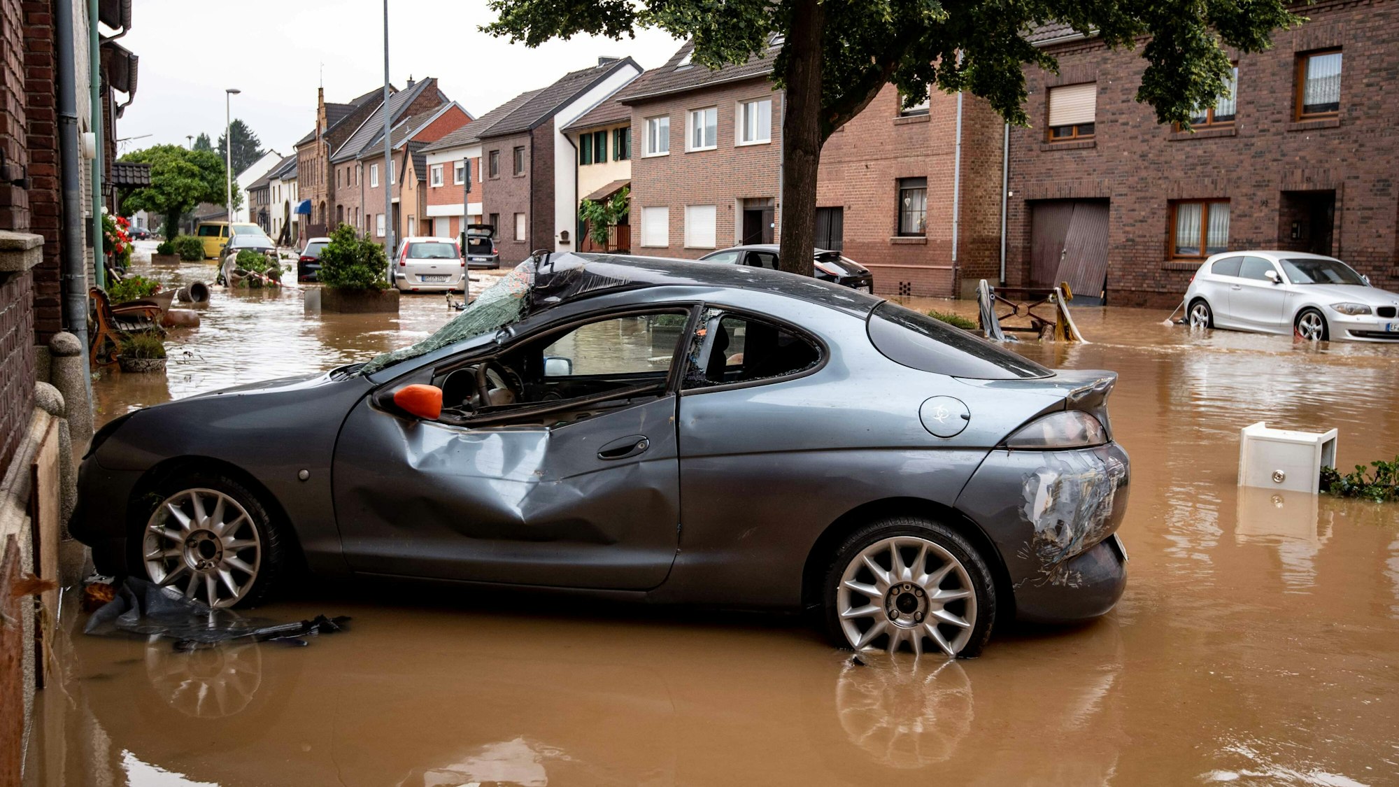 Ein zerstörtes Auto steht in einer überfluteten Straße im Ortsteil Blessem.