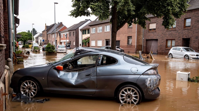 Ein zerstörtes Auto steht in einer überfluteten Straße im Ortsteil Blessem.