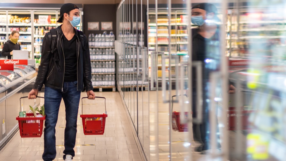 Ein Kunde geht in einem Supermarkt einkaufen und trägt dabei einen Mundschutz.