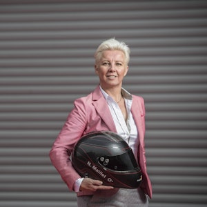 Nathalie Maillet hält einen Motorsport-Helm in der Hand und lächelt in die Kamera.