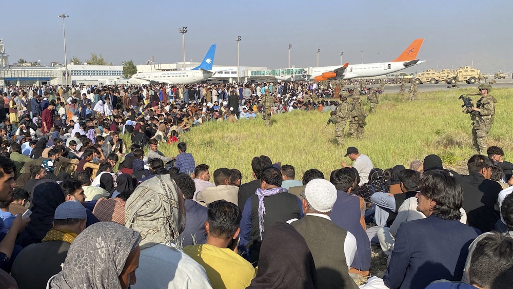 US-Soldaten bewachen eine Absperrung am Flughafen, davor drängeln sich Tausende Menschen.