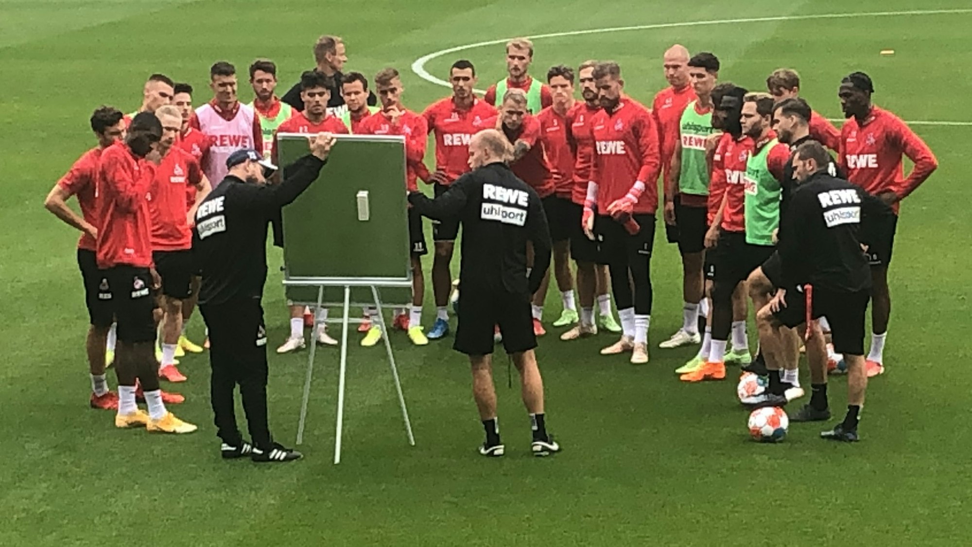 Steffen Baumgart und Assistent Kevin McKenna versammeln die Mannschaft im Training des 1. FC Köln vor der Taktiktafel.