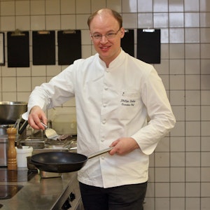 Philipp Ferber steht in der Küche und hält eine Pfanne in der Hand.
