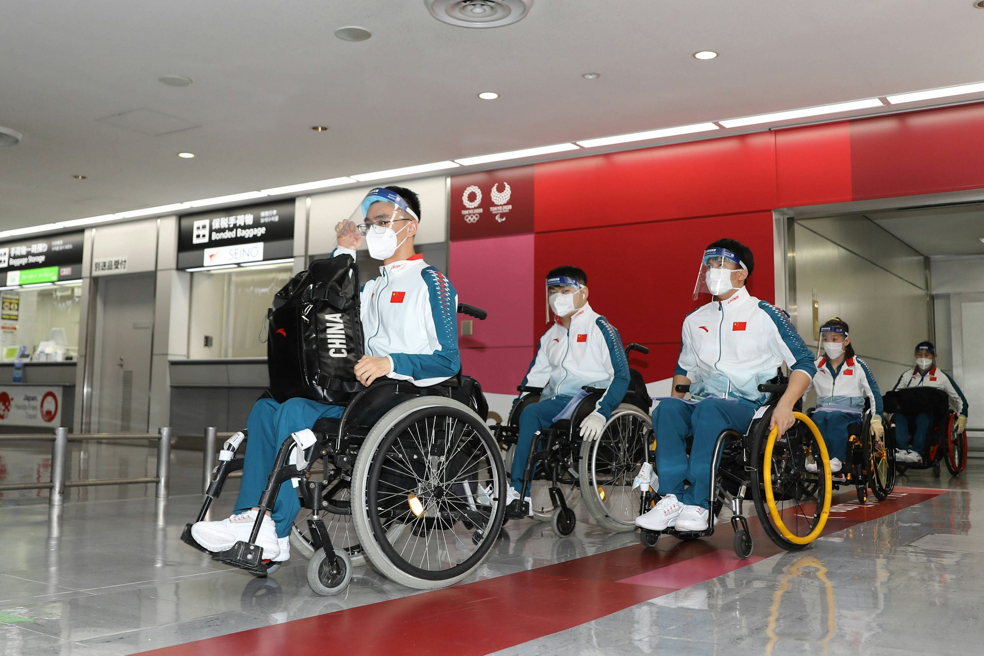 Chinesische Sportler in Rollstühlen mit Mundschutz und Plastikschutz.