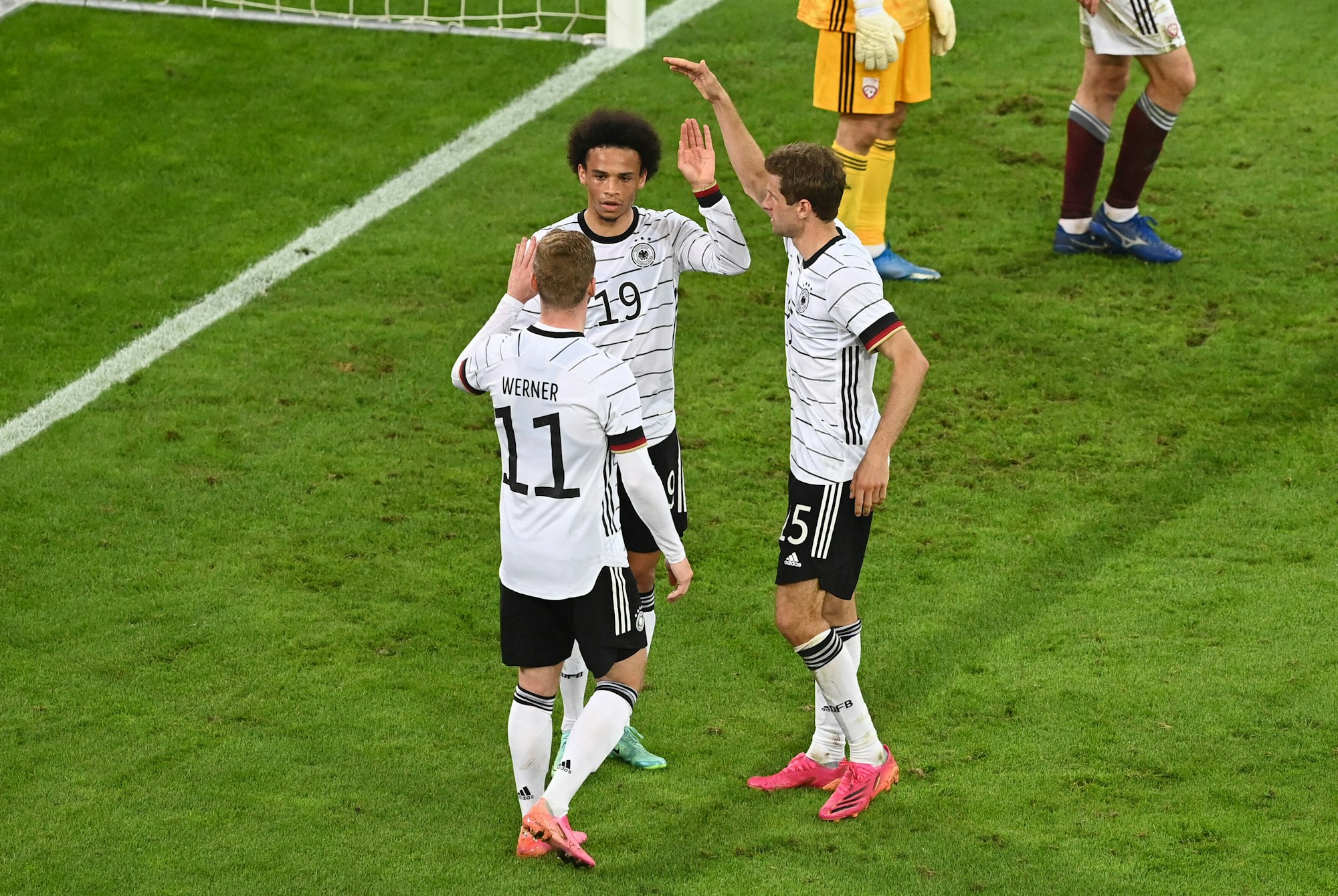 Thomas Müller, Leroy Sané und Thomas Müller stehen zusammen auf dem Feld im Trikot der deutschen Nationalmannschaft.