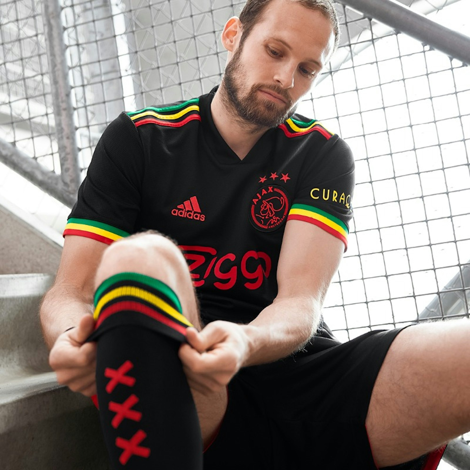 Ein Spieler sitzt im neuen schwarzen Trikot von Ajax auf einer Treppe und zieht sich die Stutzen zurecht.