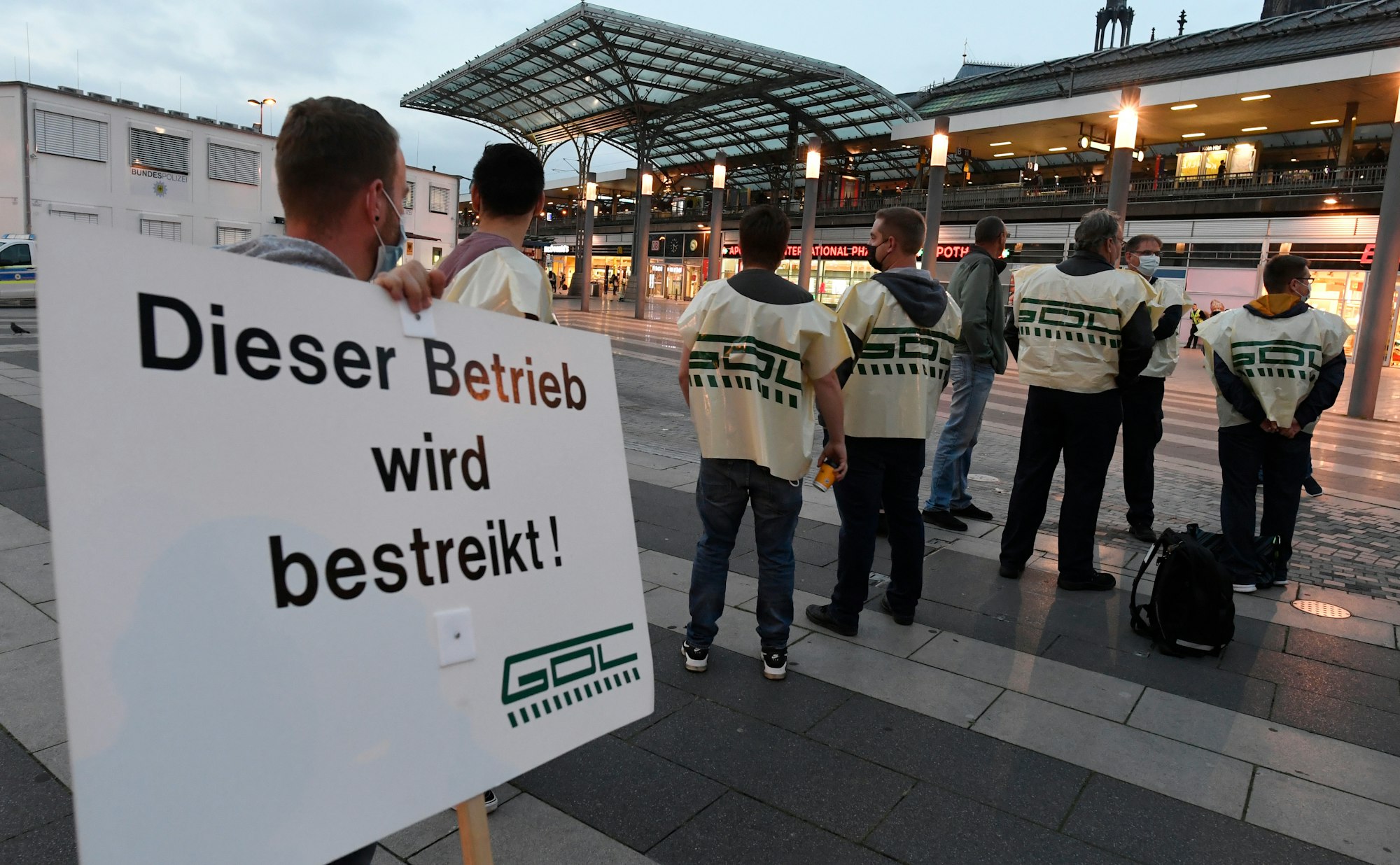 Mitglieder der Gewerkschaft der Lokführer (GDL) stehen mit einem Schild mit der Aufschrift „Dieser Betrieb wird bestreikt!“ auf dem Bahnhofsvorplatz.
