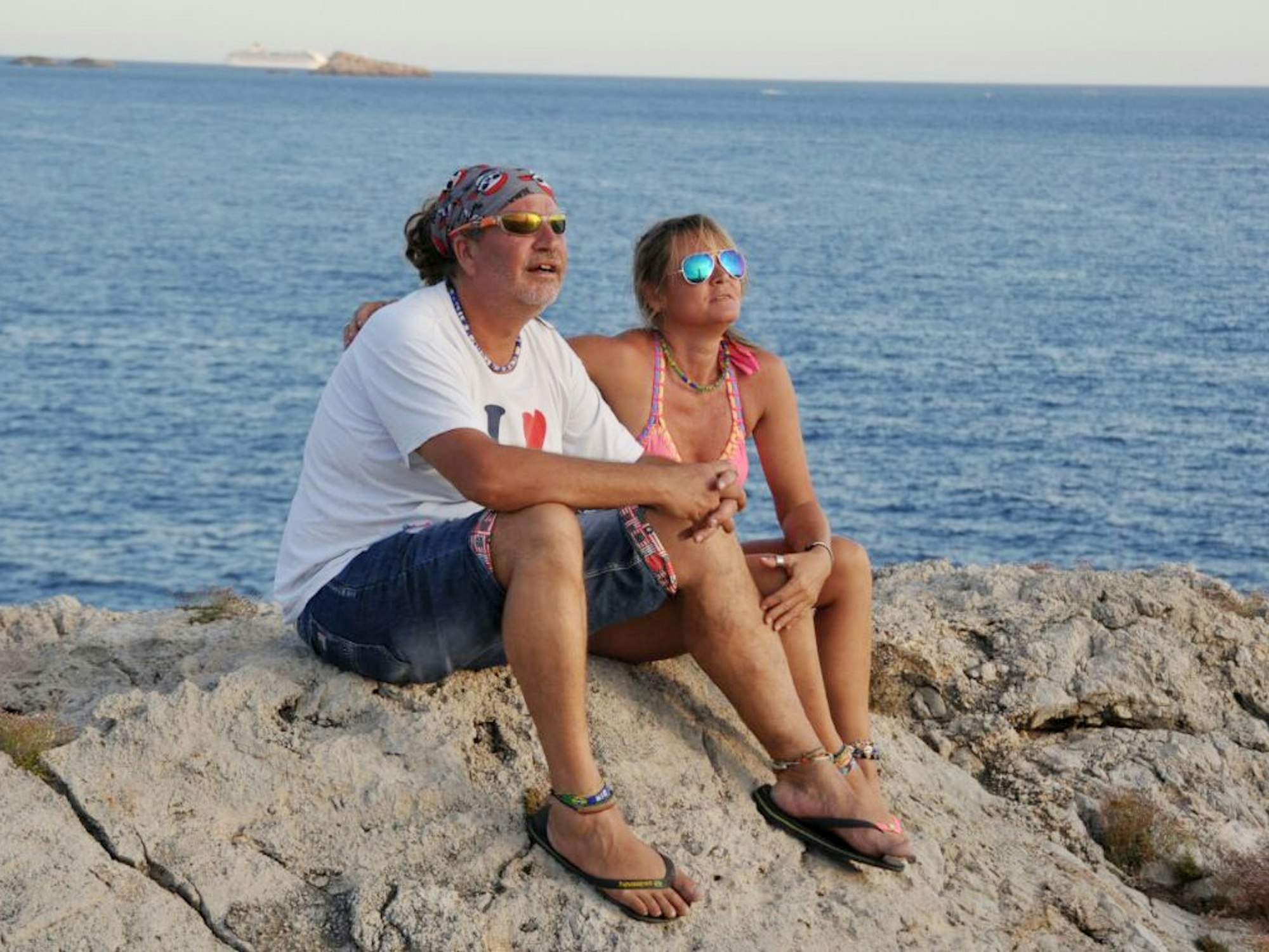 Kathrin und Tommy Mermi-Schmelz sitzen auf einem Felsen und schauen aufs Meer