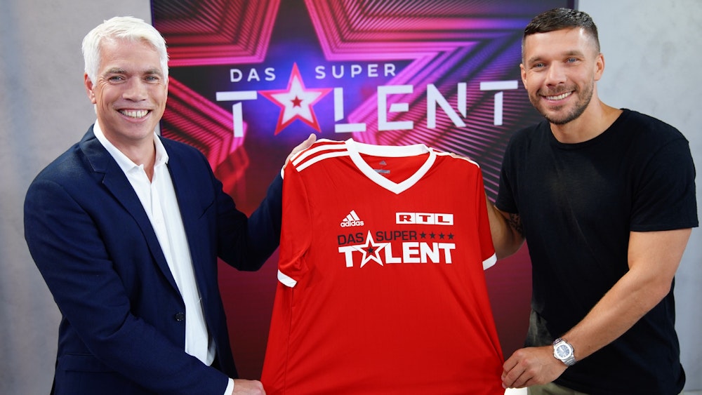 Die Freude war groß bei RTL Ende Juni, als klar war, dass Fußball-Weltmeister Lukas Podolski (r., hier zusammen mit Henning Tewes, Geschäftsführer RTL) Juror beim „Supertalent“ 2021 sein soll. Nach Podolskis positivem Corona-Test ist der weitere Plan für die Produktion nun aber offen.