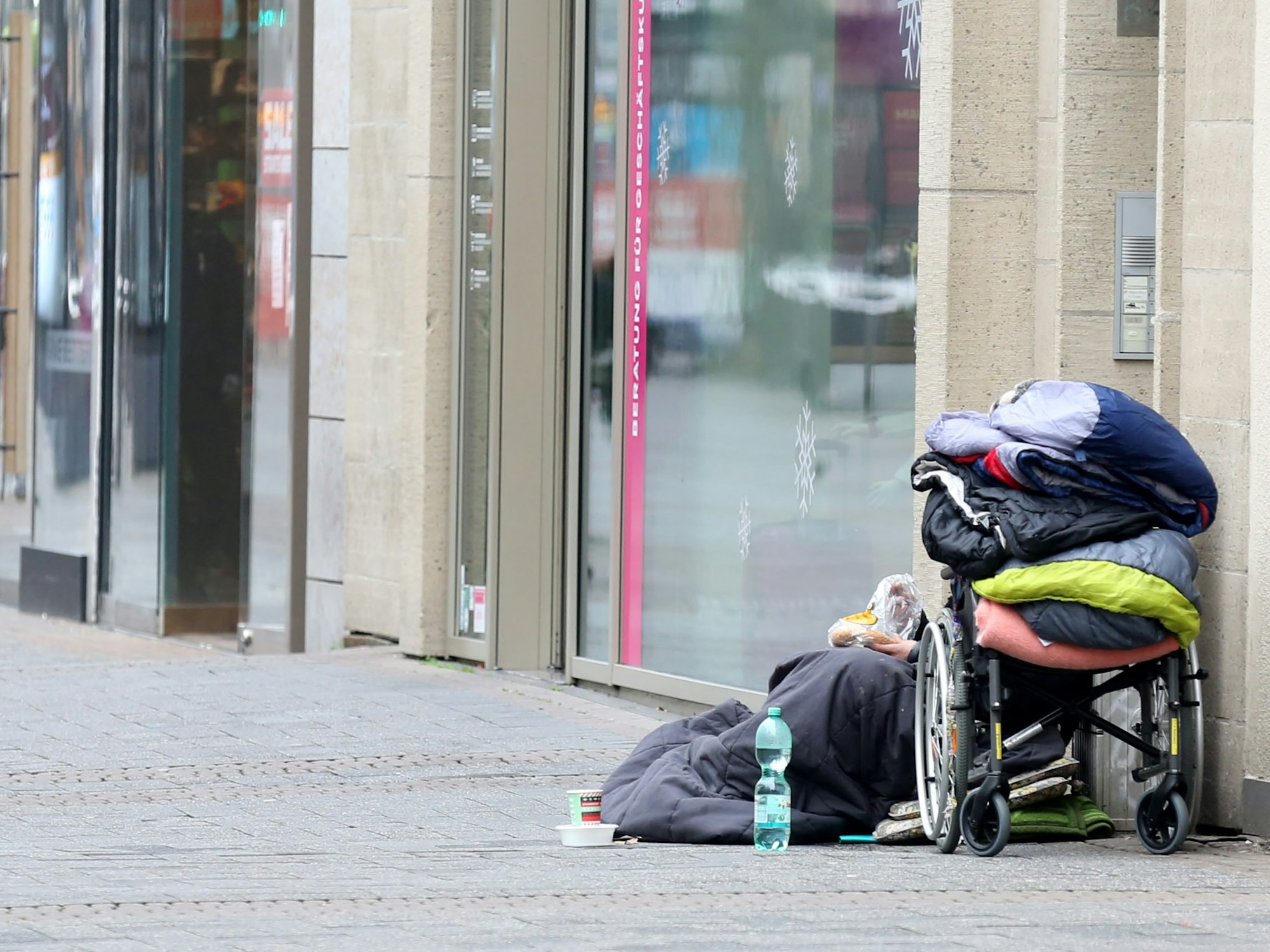 Ein Obdachloser sitzt in der Kölner Fußgängerzone vor einem Geschäft.