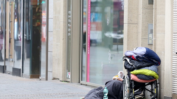 Ein Obdachloser sitzt in der Kölner Fußgängerzone vor einem Geschäft.