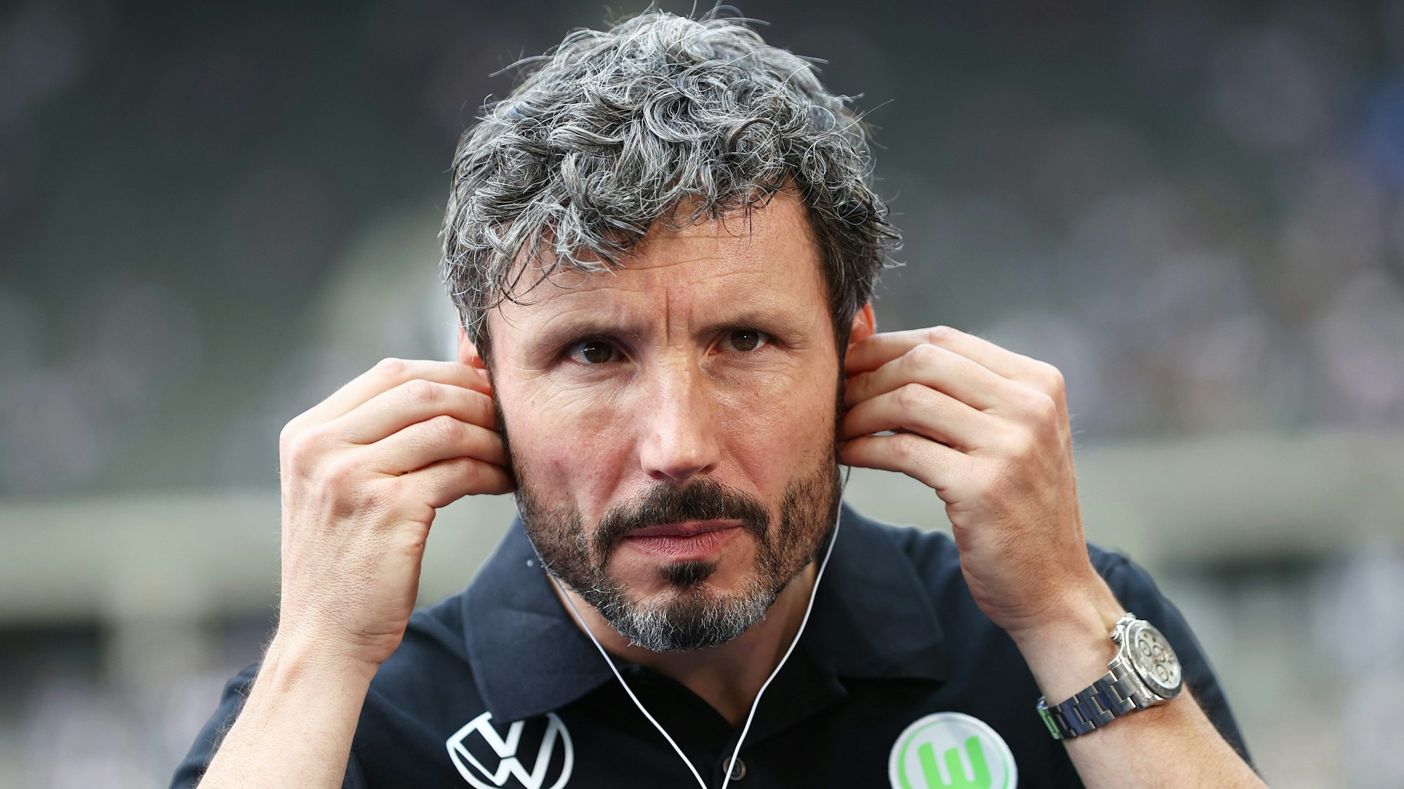 Wolfsburgs Trainer Mark van Bommel setzt Kopfhörer vor einem Interview auf.