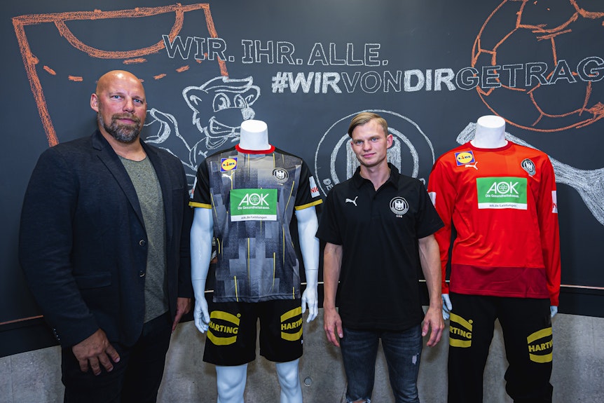 Der deutsche Nationalspieler Timo Kastening und DHB-Sportvorstand Axel Kromer stehen neben Modepuppen, die das neue Mannschafts- und Torwarttrikot tragen.