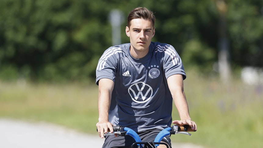 Gladbachs Nationalspieler Florian Neuhaus, hier zu sehen bei einer Radtour während des DFB-Trainingslagers in Herzogenaurach am 17. Juni 2021. Neuhaus sitzt auf einem Rand und schaut in die Kamera.