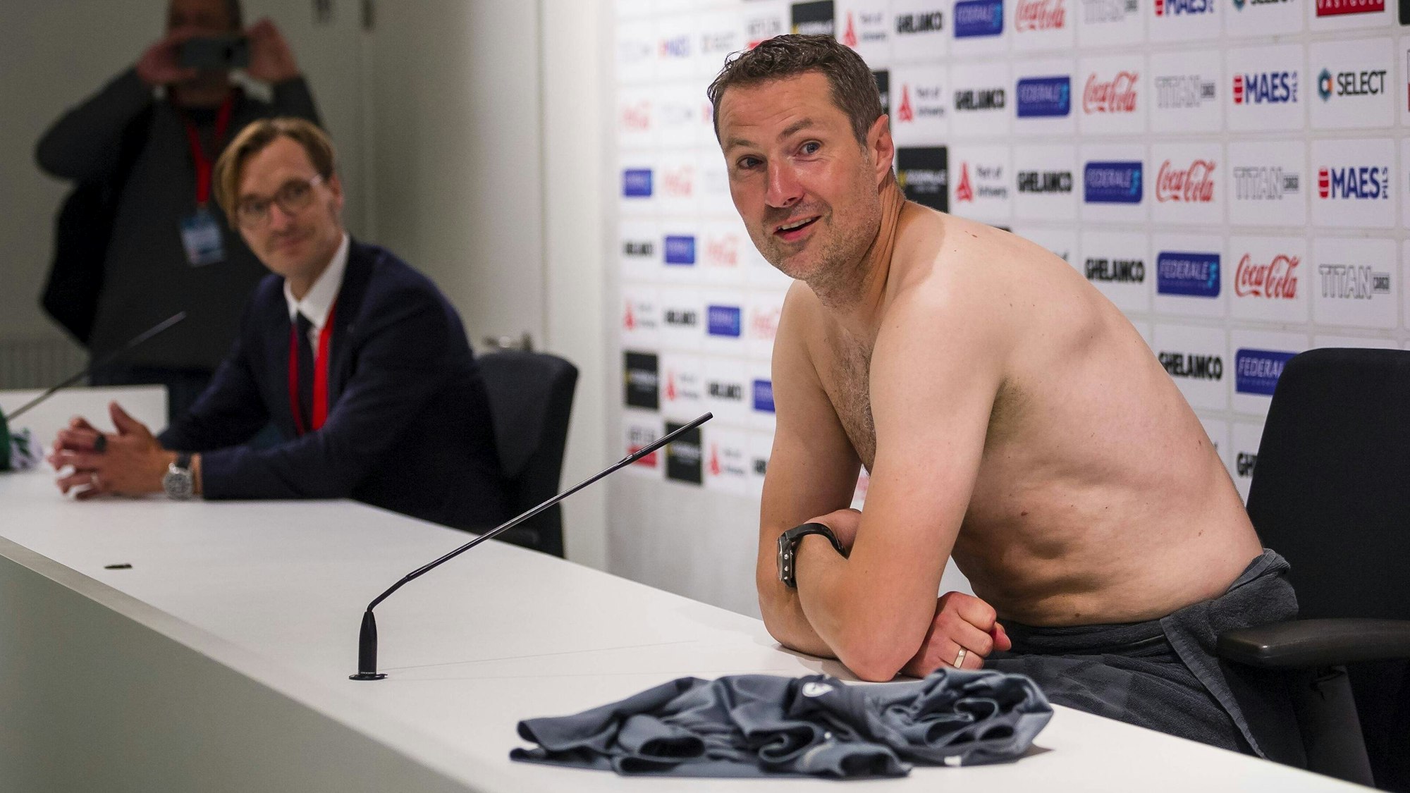 Brian Priske spricht mit nacktem Oberkörper auf der Pressekonferenz von Royal Antwerpen.
