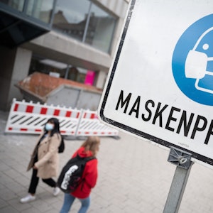 Zwei Passantinnen gehen in der Fußgängerzone hinter einem Schild vorbei, auf dem «Maskenpflicht» steht.