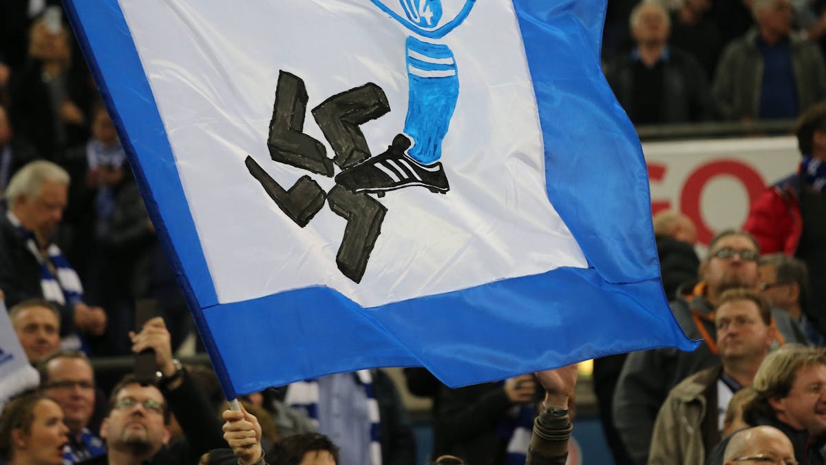 Auf einer Fahne ist ein Schalke-Wappen und ein Fuß zu sehen. Der Fuß zertritt ein Hakenkreuz.