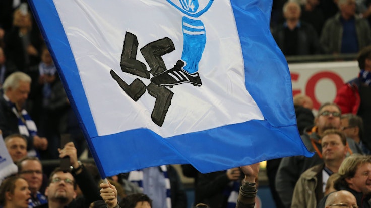 Auf einer Fahne ist ein Schalke-Wappen und ein Fuß zu sehen. Der Fuß zertritt ein Hakenkreuz.