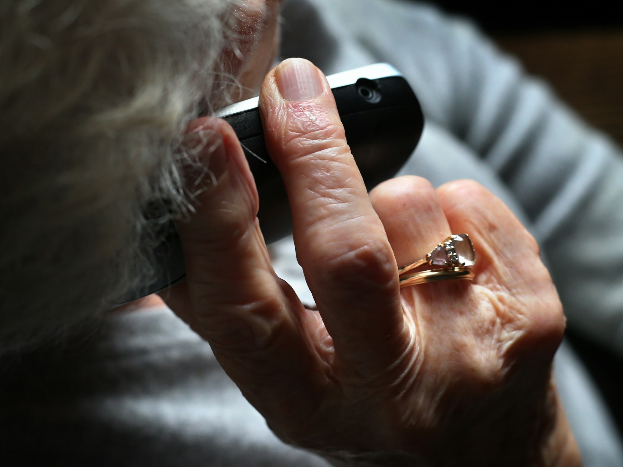 Eine ältere Frau, die einen wertvollen Ring am Finger trägt, telefoniert mit einem schnurlosen Festnetztelefon.