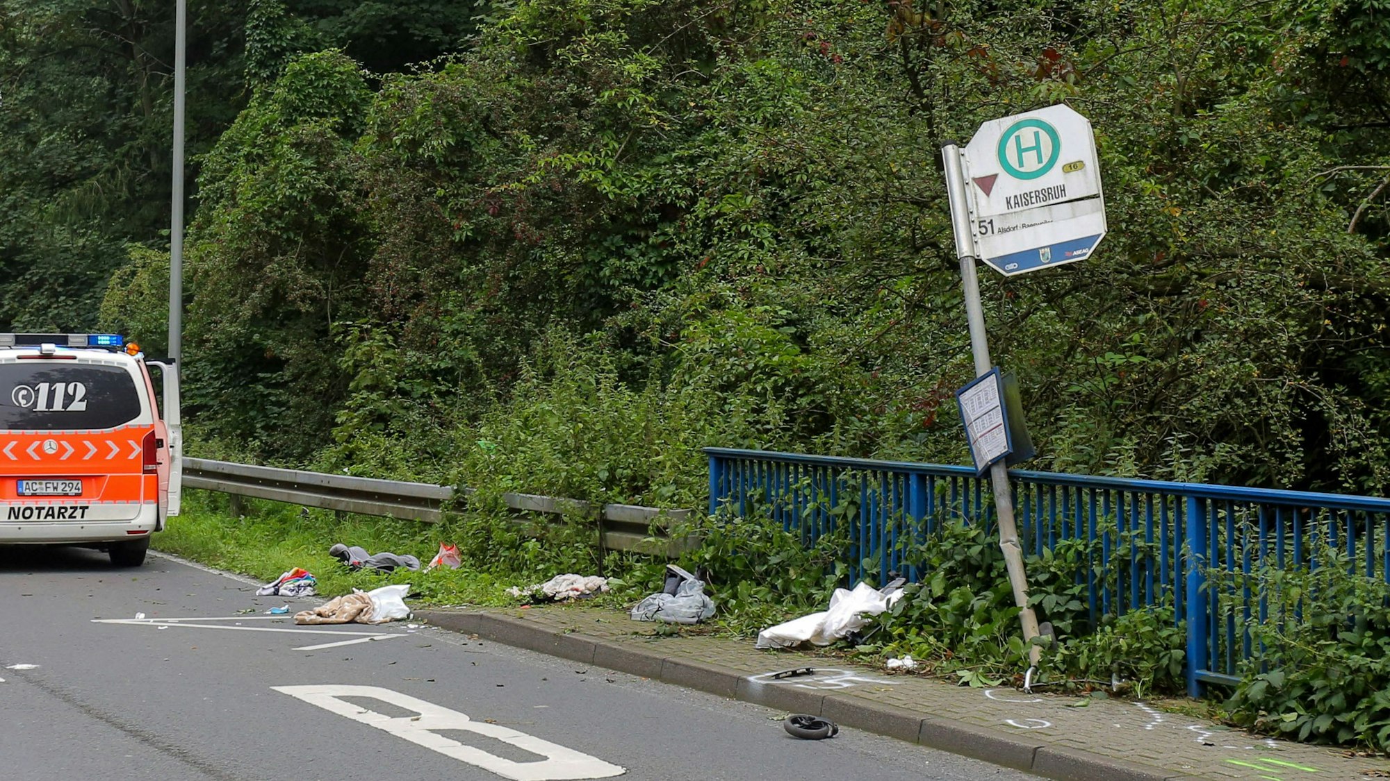 Das Schild einer Bushaltestelle ist umgebogen, ein kleines Rad und andere Gegenstände liegen davor verstreut.