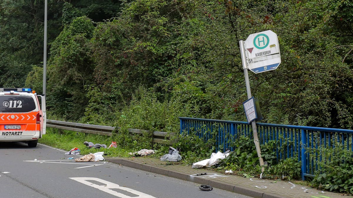Das Schild einer Bushaltestelle ist umgebogen, ein kleines Rad und andere Gegenstände liegen davor verstreut.