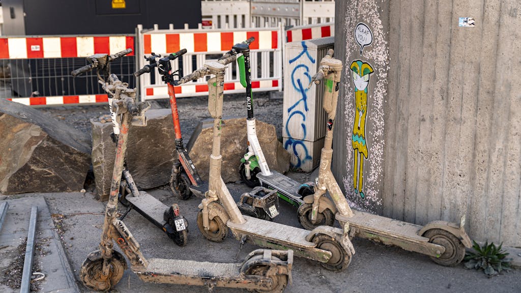 Verschlammte E-Scooter stehen an einer Mauer in Köln.