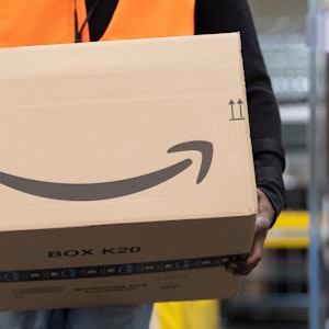 Ein Sortiermitarbeiter von Amazon trägt in einem Verzeilzentrum ein Paket.