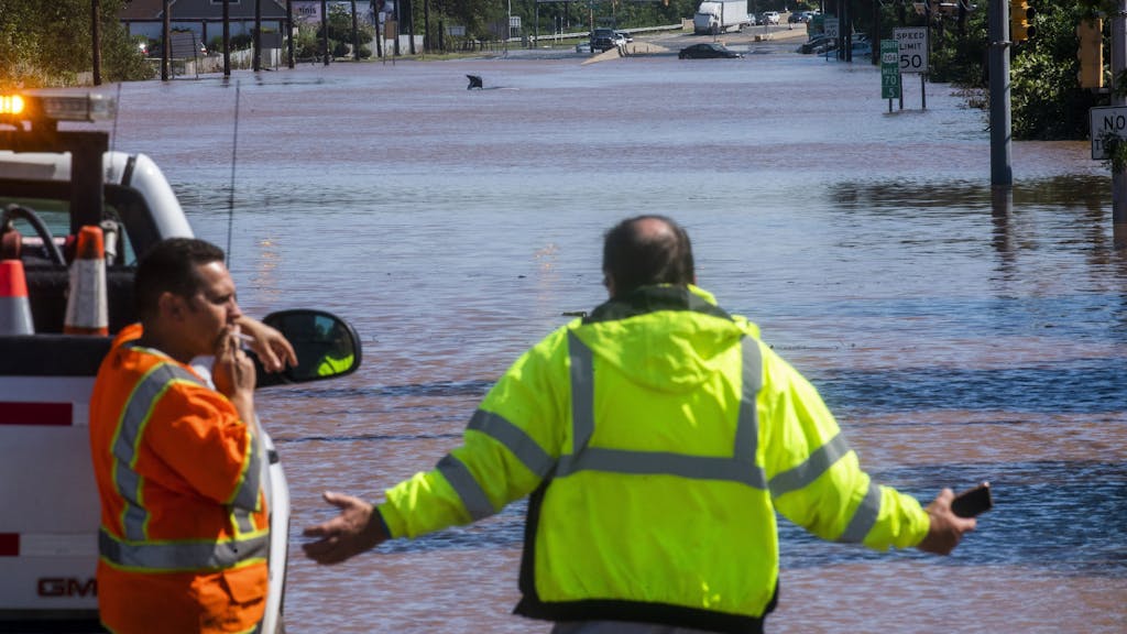 Menschen stehen an der überfluteten Bundesstraße 206 in New Jersey. Im Hintergrund sind überflutete Autos zu sehen.