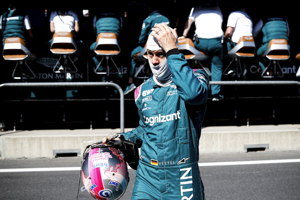 Sebastian Vettel mit Helm in der Hand und Gesichtsmaske auf dem Kopf fasst sich an den Kopf.