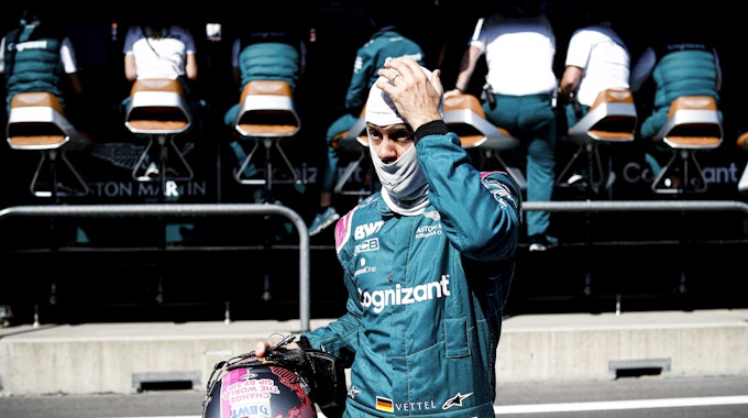 Sebastian Vettel mit Helm in der Hand und Gesichtsmaske auf dem Kopf fasst sich an den Kopf.