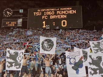 Auf der Anzeigetafel steht, dass 1860 mit 1:0 gegen Bayern gewonnen hat. Darunter freuen sich die Fans der Löwen.