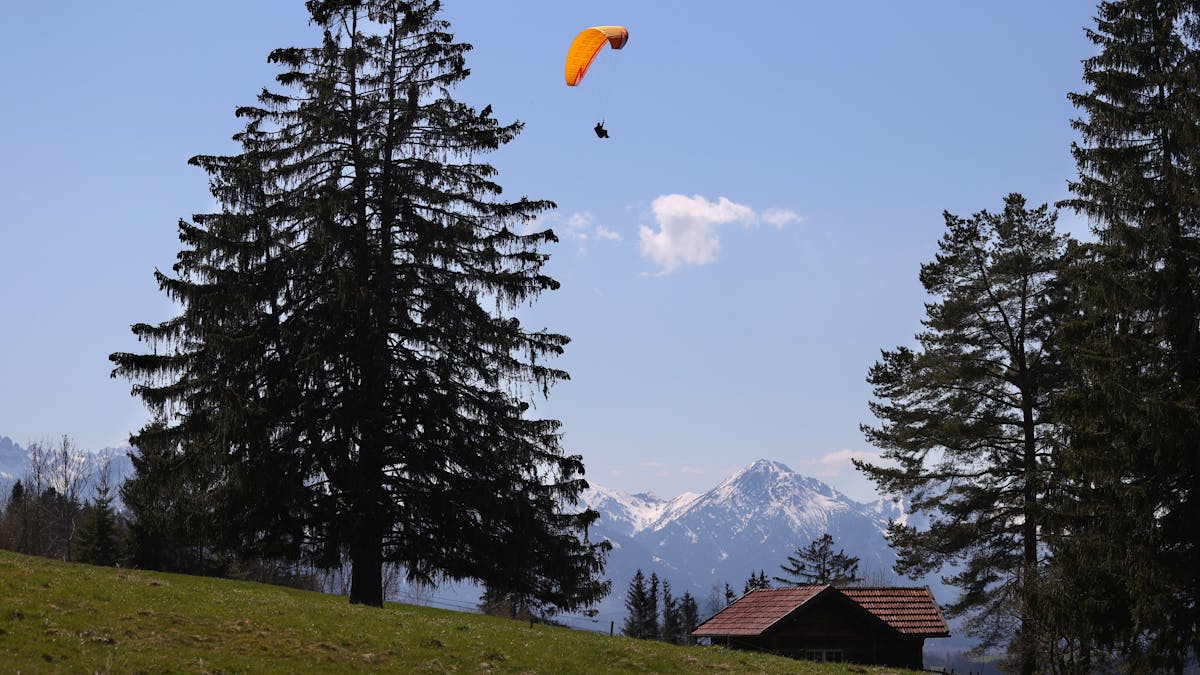 Ein Gleitschirmflieger über einer Hütte in Bayern.