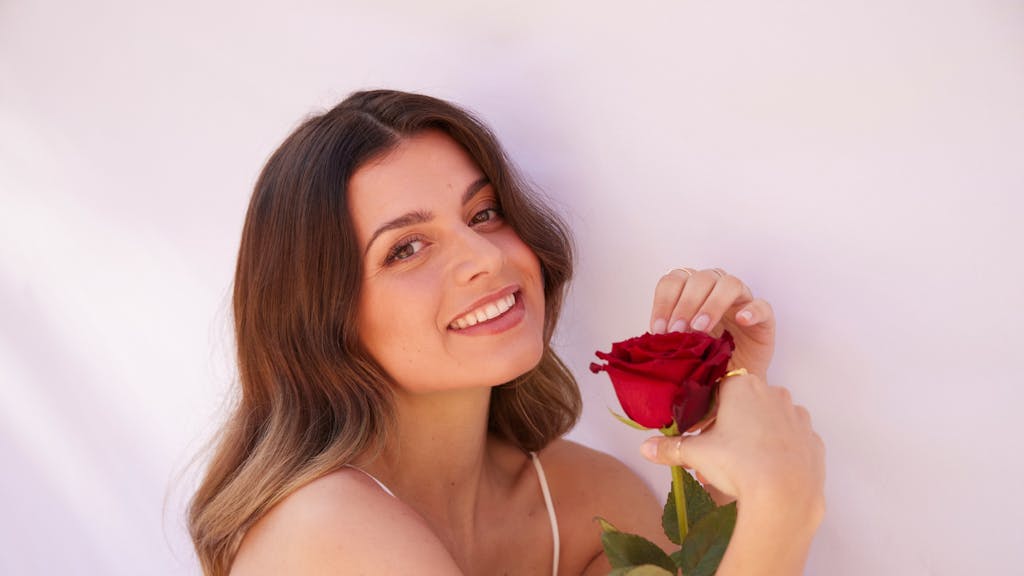 „Bachelorette“ Maxime lächelt in die Kamera und hält eine Rose in der Hand.
