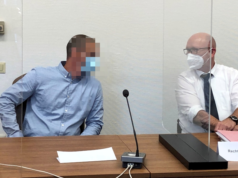 Ein Kölner Polizist sitzt auf der Anklagebank im Kölner Landgericht und spricht mit seinem Anwalt.
