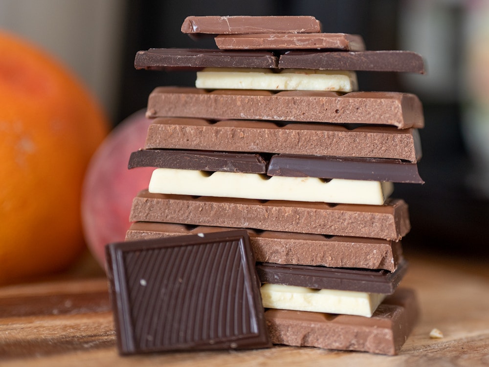 Stücke von Vollmilchschokolade, weißer Schokolade und Zartbitterschokolade liegen auf einem Holzbrett in der Küche.